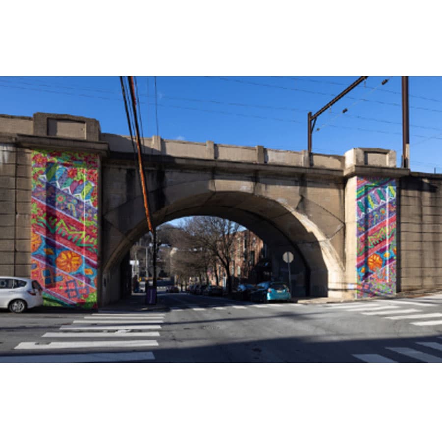 A colorful mural adorns a stone bridge over a quiet street.