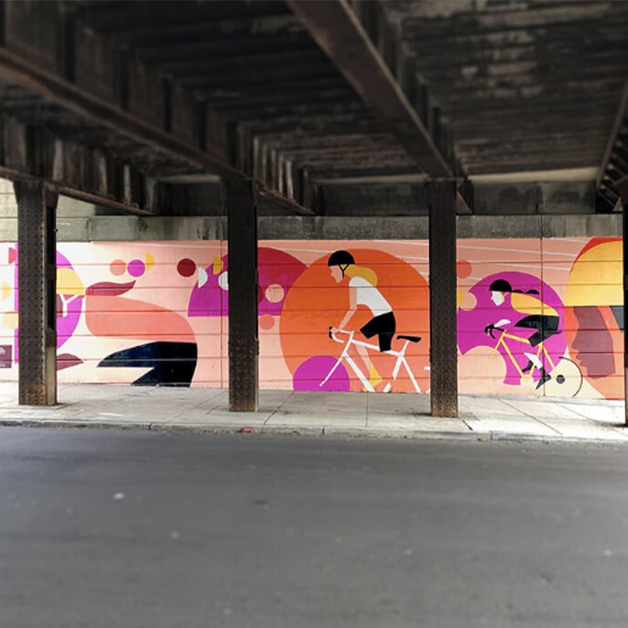 A mural of two cyclists in vibrant colors under an overpass.