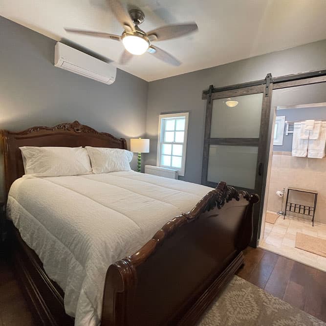 A cozy bedroom featuring a wooden bed, a ceiling fan, and an adjoining bathroom with a sliding door.