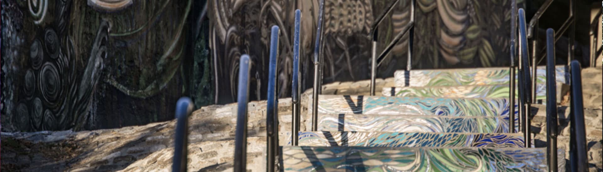 Colorful tiled stairs lead upwards against a textured mural backdrop.