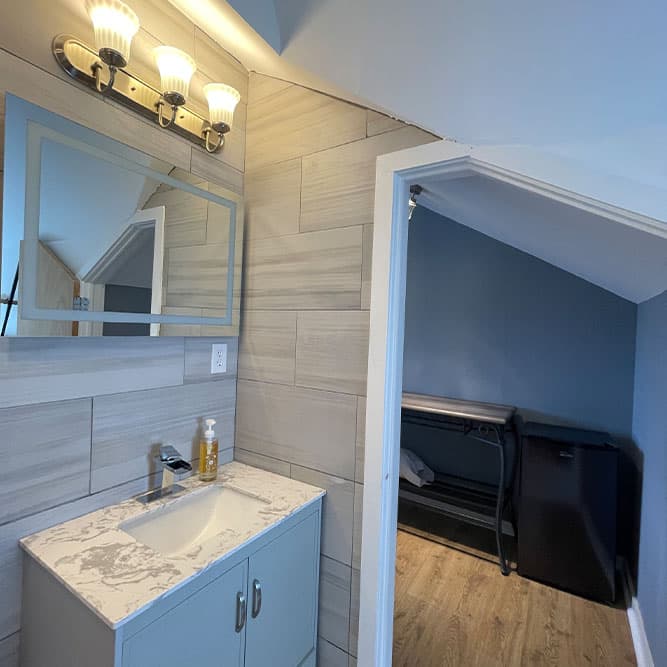 A modern bathroom featuring a sink with a mirror and three light fixtures, leading to a small adjoining room.