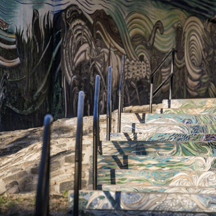 Colorful, painted stairs ascend beside a mural depicting abstract natural forms.