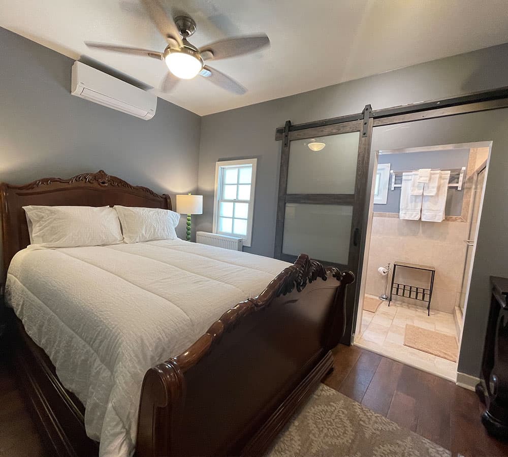 A cozy bedroom featuring a wooden bed, ceiling fan, and an adjoining bathroom.
