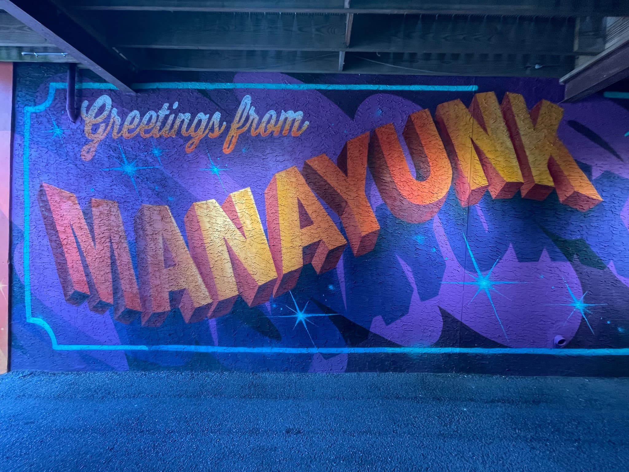 Colorful mural reading "Greetings from MANAYUNK" on a textured wall.