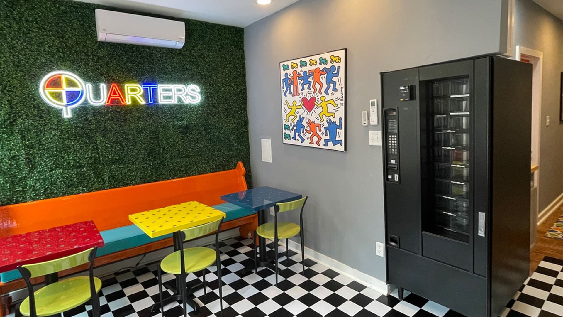 Colorful seating and a neon sign decorate a modern snack area with a vending machine.