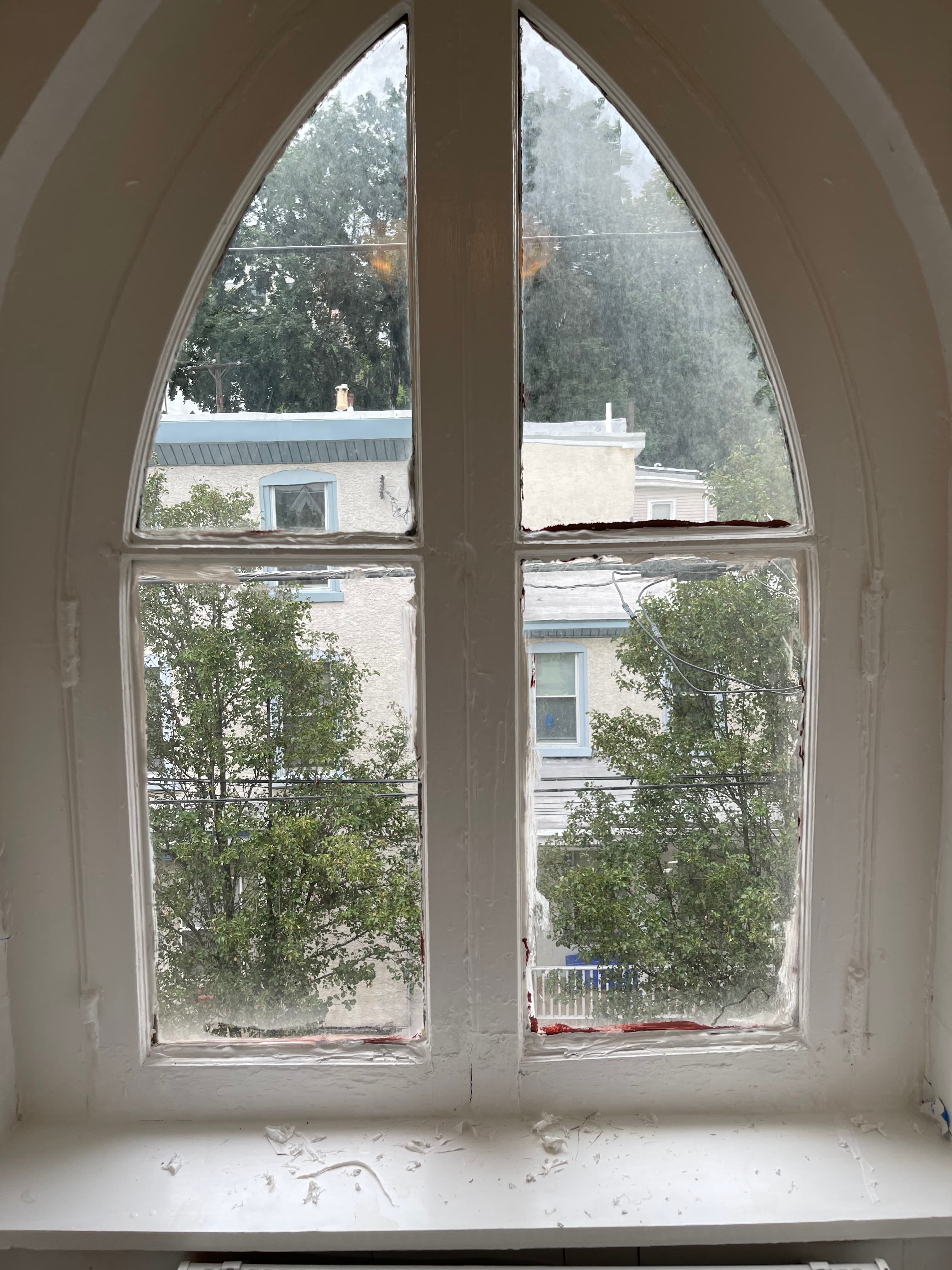 Close-up of an arched window with a white frame and multiple panes, offering a view of trees and buildings through the glass.
